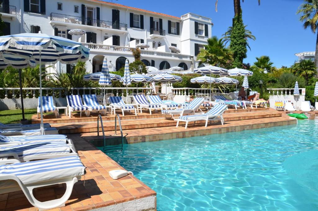 een zwembad met blauwe en witte stoelen en parasols bij Hotel des Mimosas in Juan-les-Pins