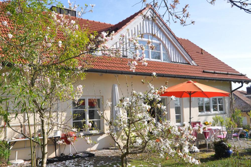 une maison blanche avec un parasol orange devant elle dans l'établissement Bed and Breakfast Bavaria München, à Icking