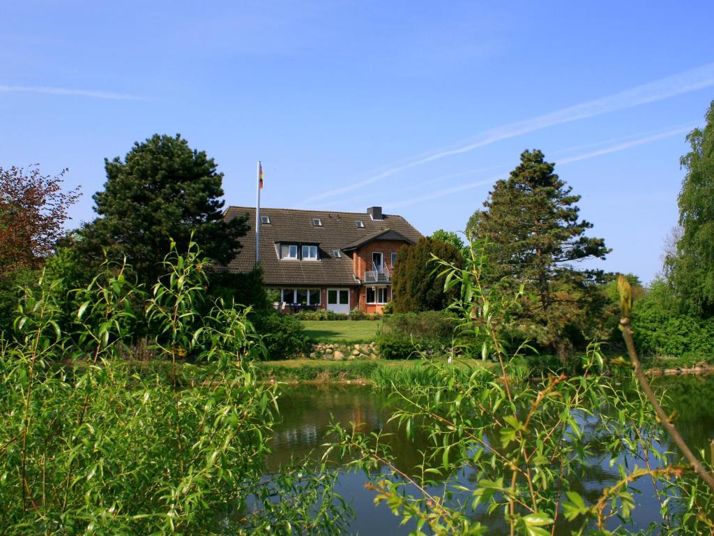 a house on the water with trees in the foreground at Landhaus Jägerhof in Börnsdorf
