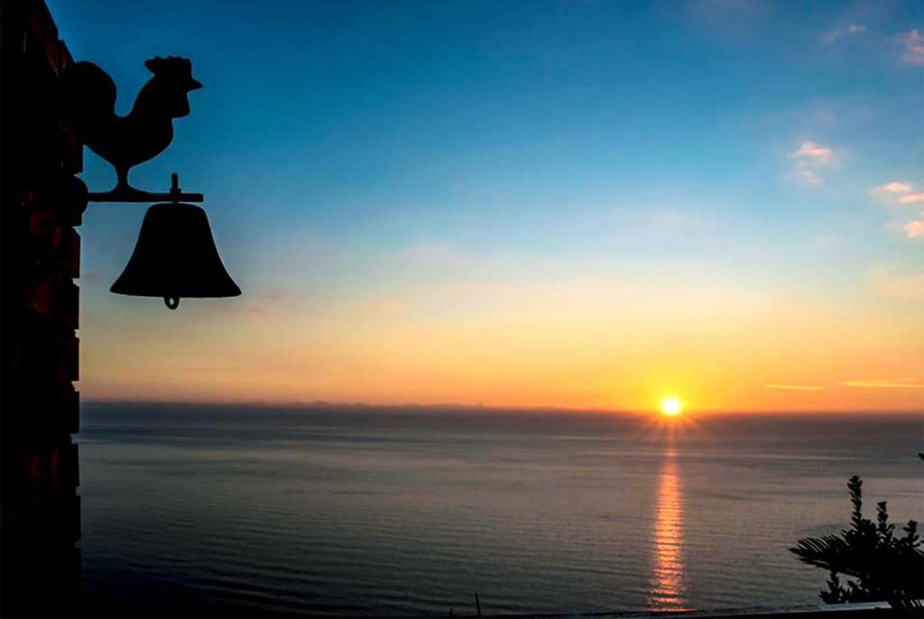 una campana con un gallo delante de una puesta de sol en Agriturismo Principe di Vallescura, en Pisciotta