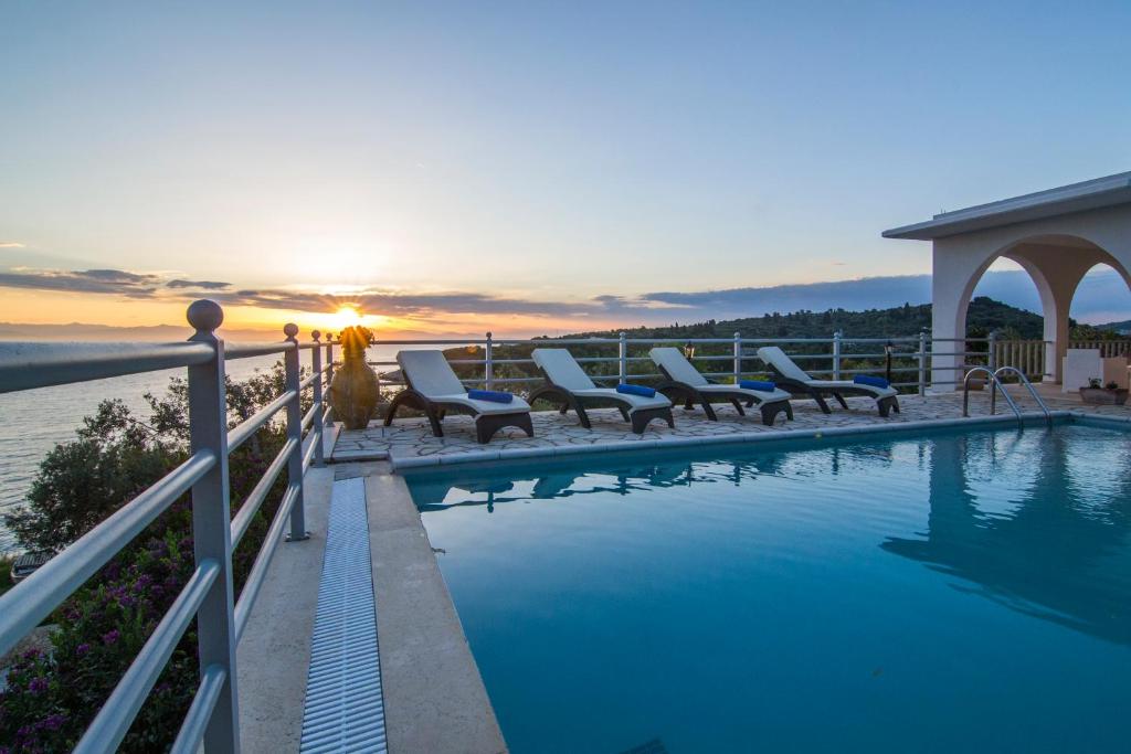 a swimming pool with chairs and the sunset in the background at Lioniskari in Porto Ozias