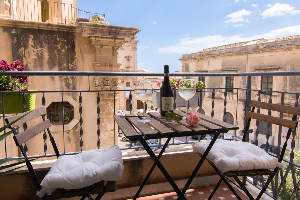 a table with a bottle of wine and two chairs on a balcony at Maison Ortigia in Syracuse