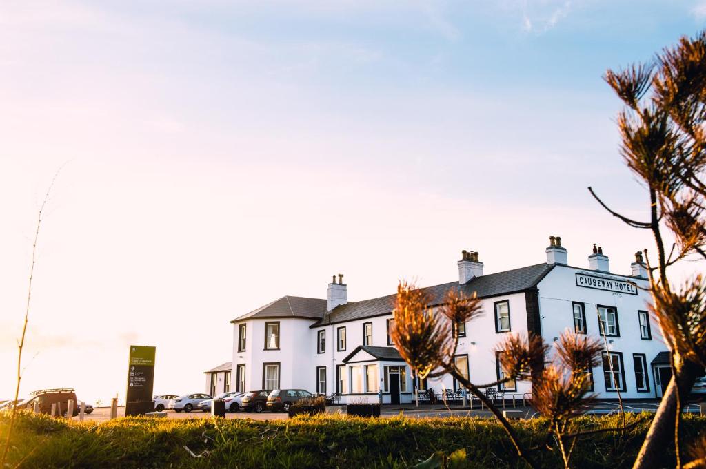 un grand bâtiment blanc avec des voitures garées dans un parking dans l'établissement Causeway Hotel, à Bushmills