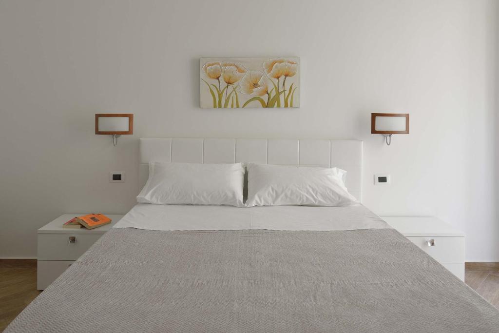 ポルト・エンペードクレにあるCavaliere Costaの白いベッドと壁に絵画が飾られたベッドルーム1室