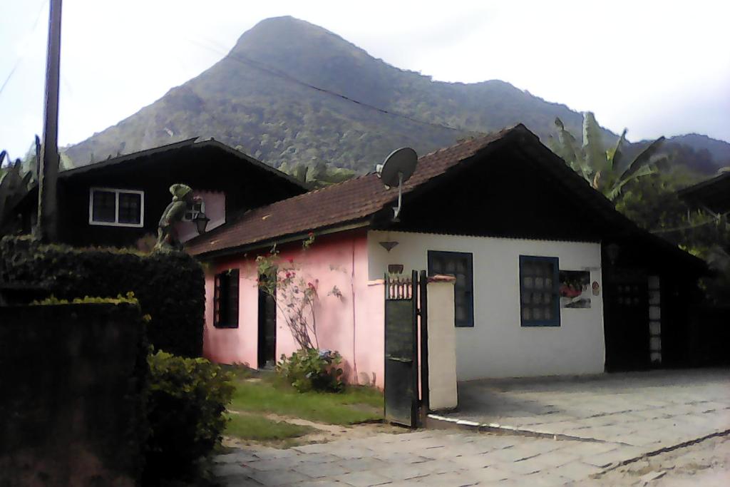 a pink and white house with a mountain in the background at Pousada Bom Bocado in São Pedro da Serra