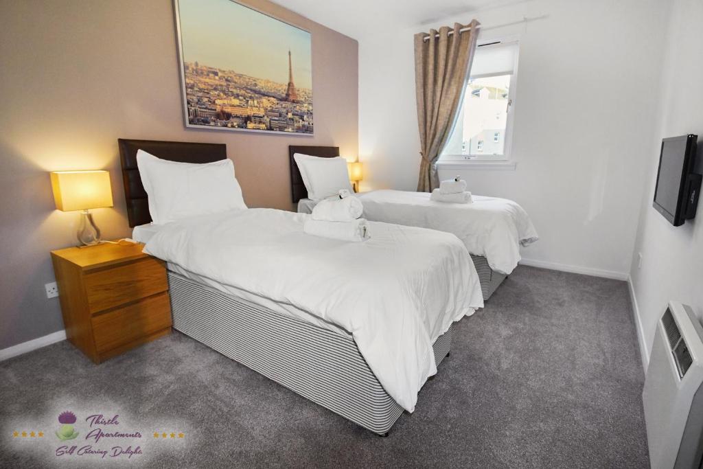 a bedroom with two beds with white sheets and a window at Thistle Apartments-City View Apartment in Aberdeen