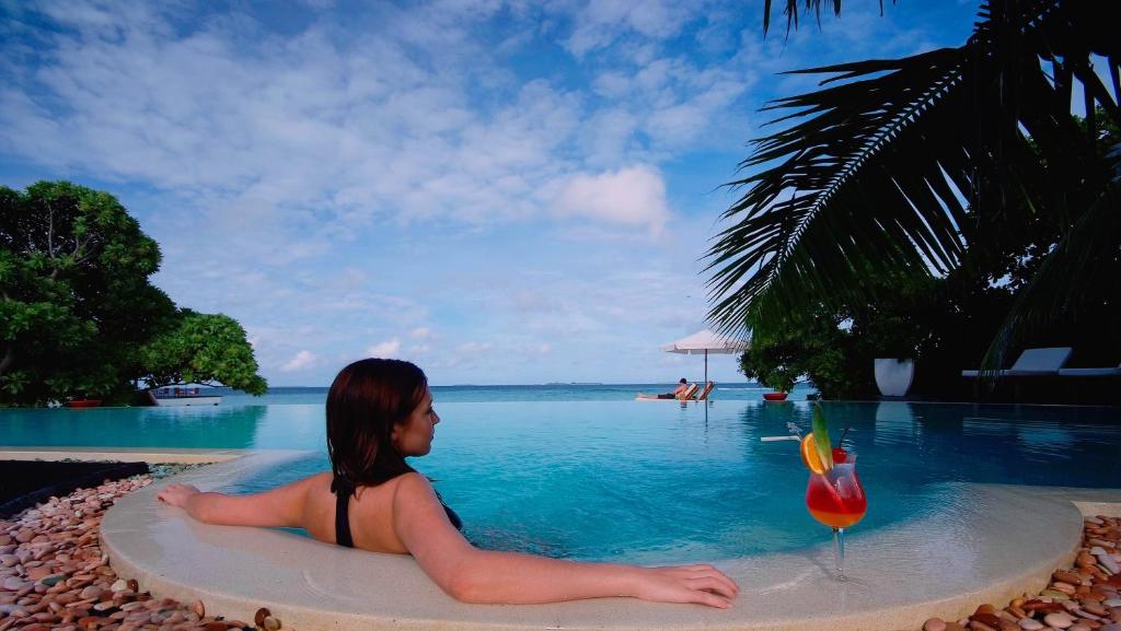 a woman sitting in a pool next to a drink at Adaaran Prestige Water Villas - with Dine around Premium All inclusive - 24 hours in Raa Atoll