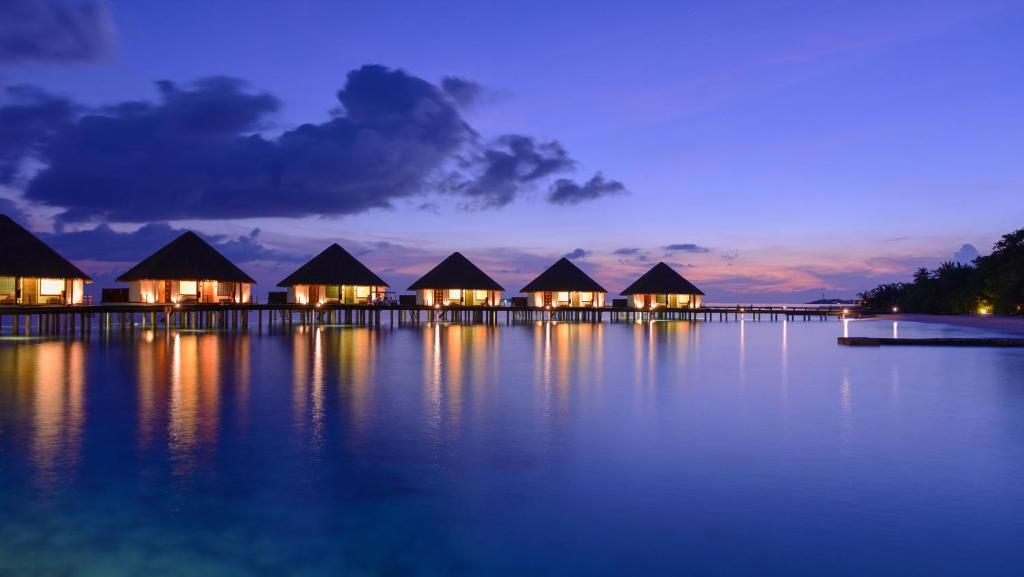 a row of huts on the water at night at Adaaran Prestige Water Villas - with Dine around Premium All inclusive - 24 hours in Raa Atoll