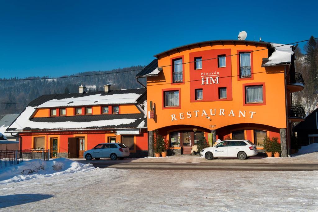 un bâtiment orange avec deux voitures garées devant lui dans l'établissement Penzion HM, à Oščadnica