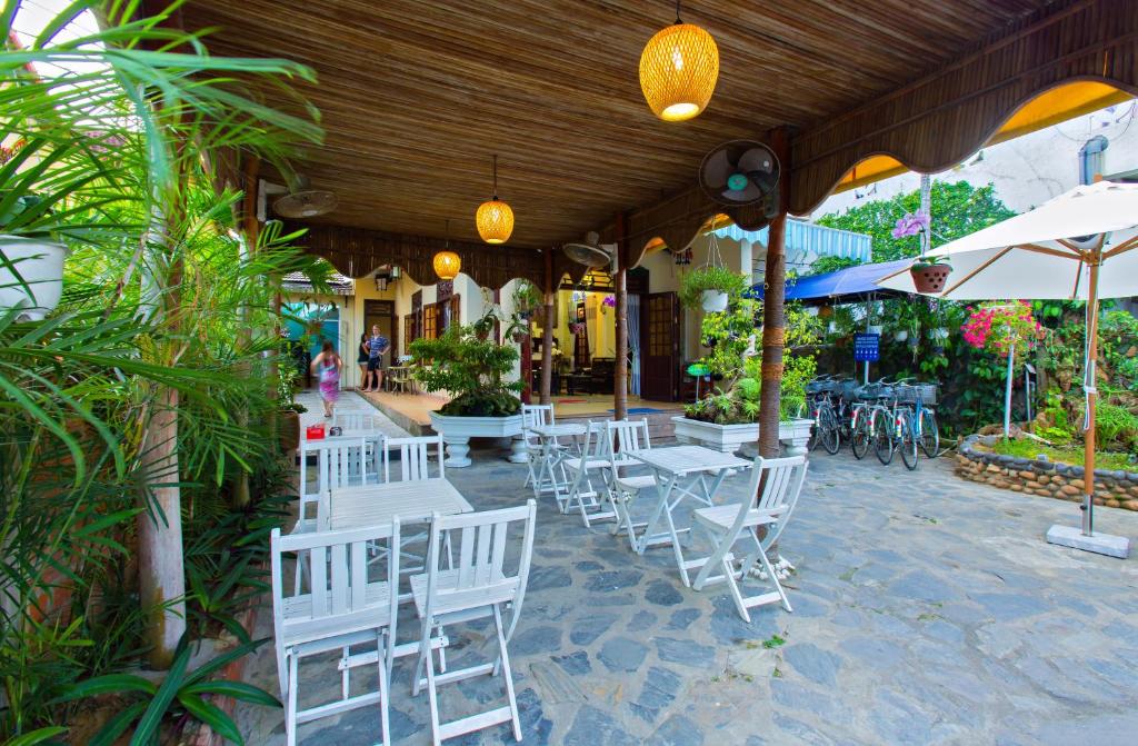 a patio with white chairs and tables and umbrellas at Mango Garden Hoi An Homestay in Hoi An