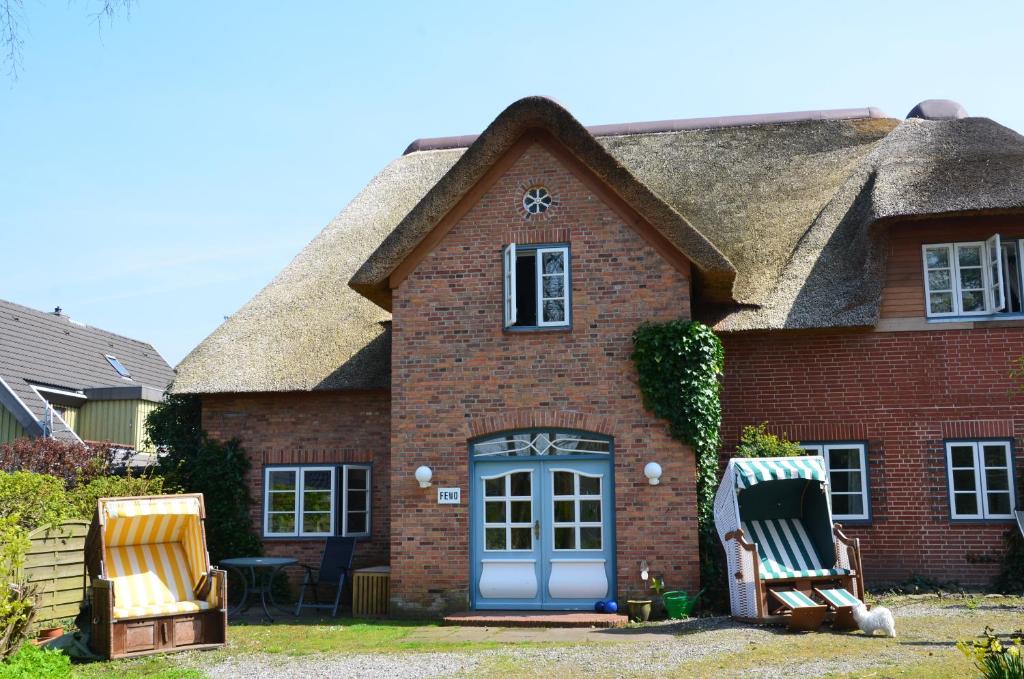 a house with two chairs and a thatch roof at Wohnen Unter Reet in Niebüll