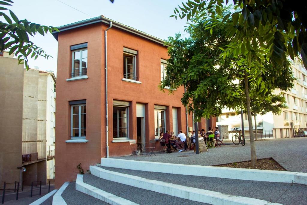 un edificio con gente sentada fuera de él en La Maison Rouge - Backpacker Hostel en Saint-Étienne