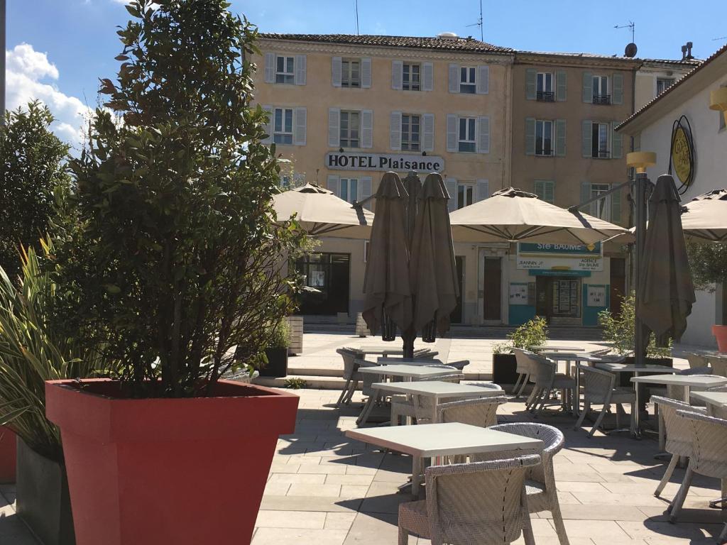 un patio con mesas, sillas y sombrillas frente a un edificio en L'Annexe Plaisance, en Saint-Maximin-la-Sainte-Baume