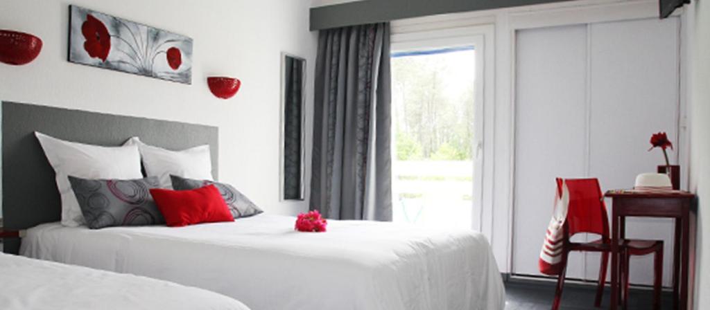 - une chambre avec 2 lits dotés d'oreillers rouges et d'une fenêtre dans l'établissement Hotel du Porge, à Le Porge