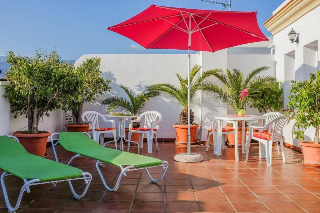 a patio with tables and chairs and a red umbrella at Apartamentos Centurión in Nerja