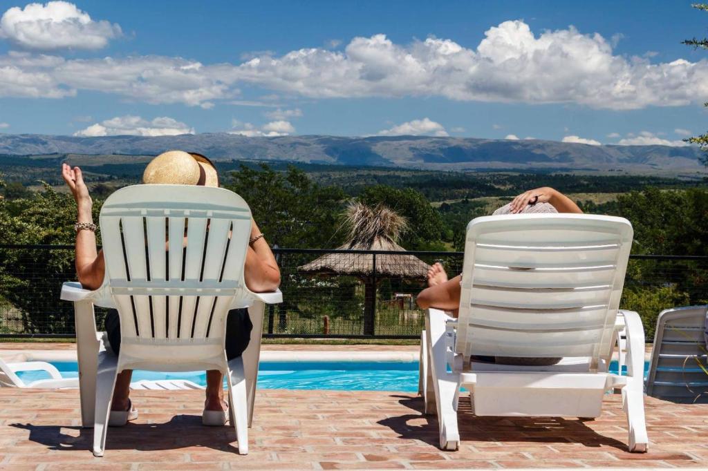 two people sitting in lawn chairs next to a pool at Cabañas & Suites Vista Hermosa in Los Reartes