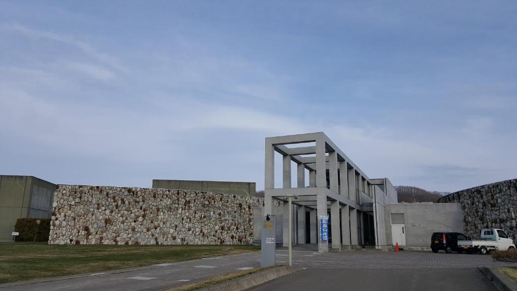 un bâtiment avec un grand mur en pierre à côté d'un parking dans l'établissement Tokachi Nauman Onsen Hotel arco, à Makubetsu