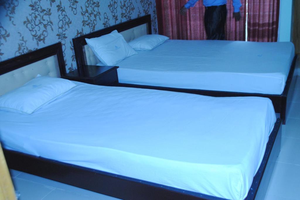2 camas en una habitación con sábanas y almohadas blancas en Shopno Bilash Holiday Suites, en Cox's Bazar