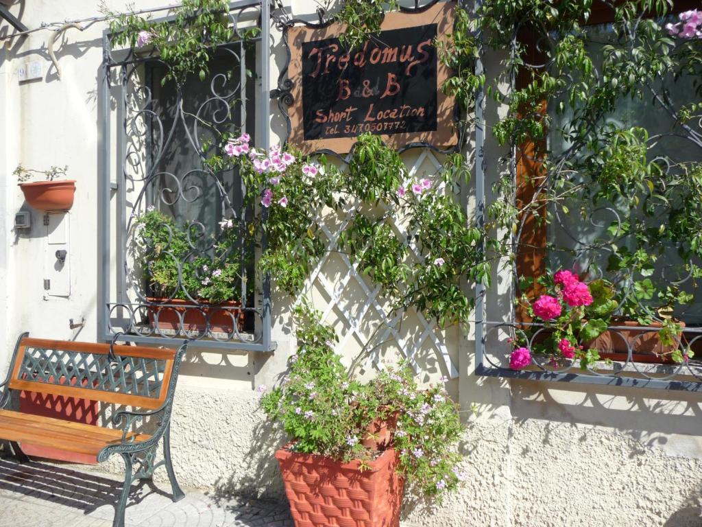 un banco sentado frente a un edificio con flores en B&B Tredomus, en Tresnuraghes