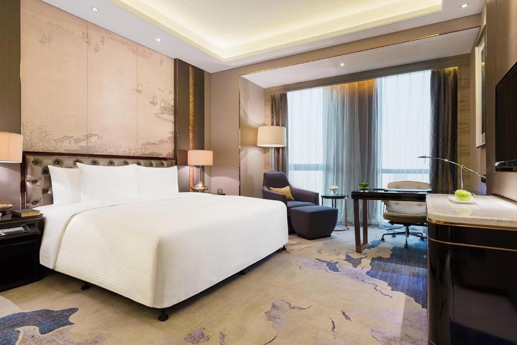 JinhuaにあるWanda Realm Jinhuaの白い大型ベッド1台、デスクが備わる客室です。