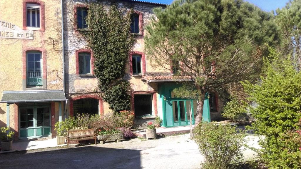 an old brick building with green doors and trees at Le Moulin de l'Abbé in Sorèze