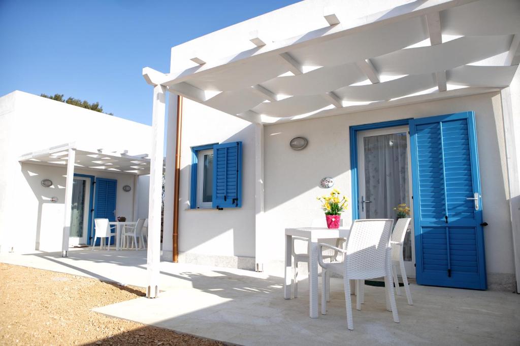 ein weißes Haus mit blauen Fensterläden sowie einem Tisch und Stühlen in der Unterkunft Plaia Resort in Favignana