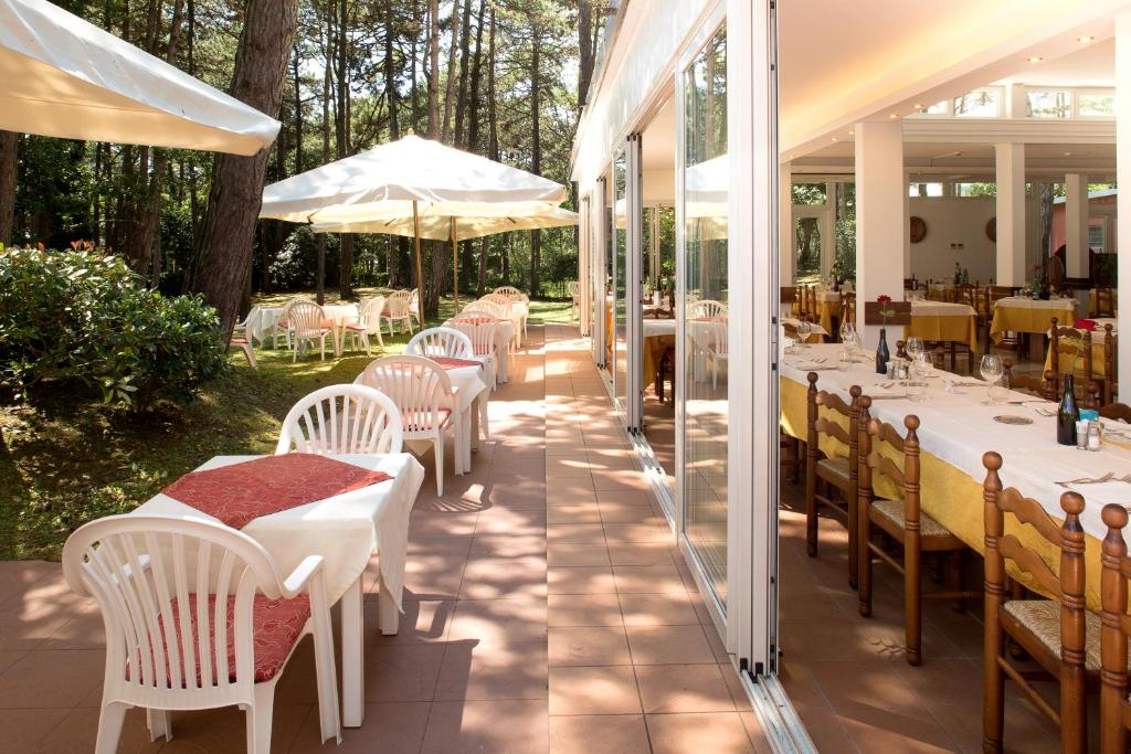 um restaurante com mesas brancas, cadeiras e árvores em Hotel San Marco em Lignano Sabbiadoro