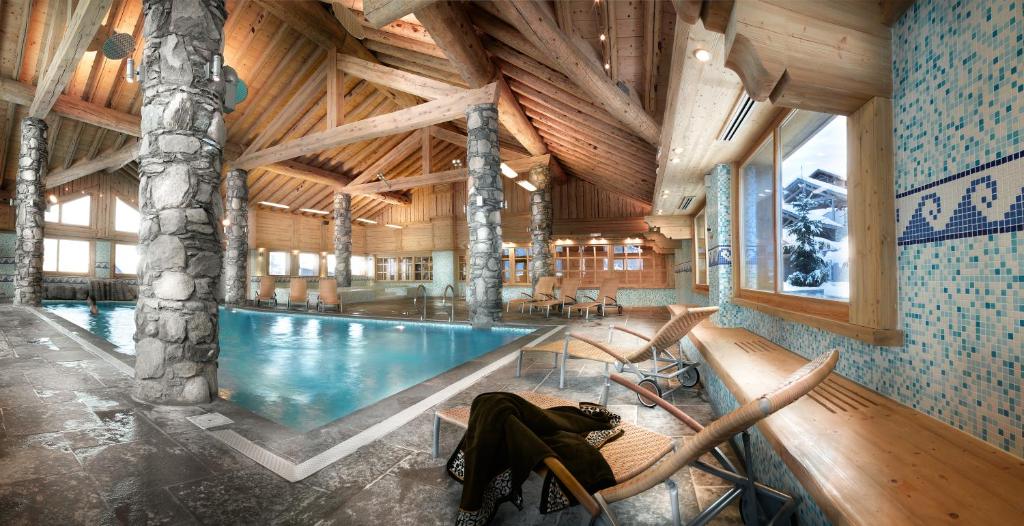 una piscina en un edificio de madera con sillas alrededor en CGH Résidences & Spas Orée Des Cimes, en Peisey-Nancroix