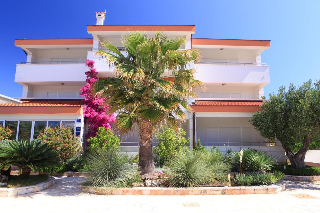 a building with a palm tree in front of it at Apartments Spirito in Rogoznica