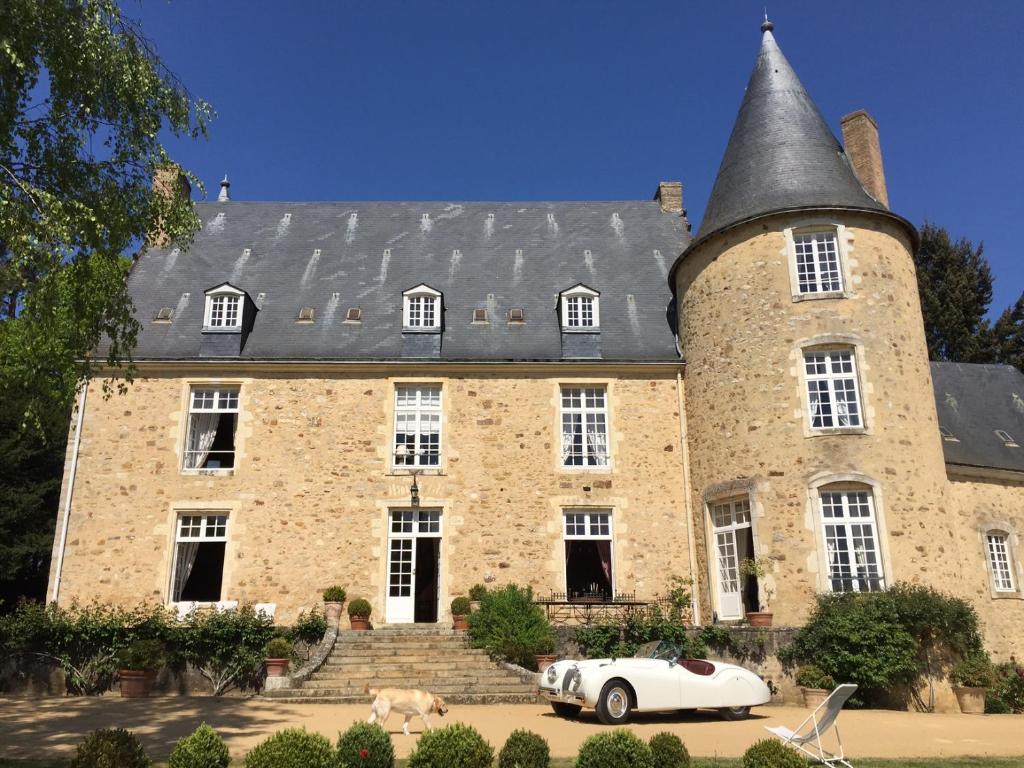 un gran edificio de piedra con un coche blanco aparcado delante en Chateau de Vaux en Yvré-lʼÉvêque