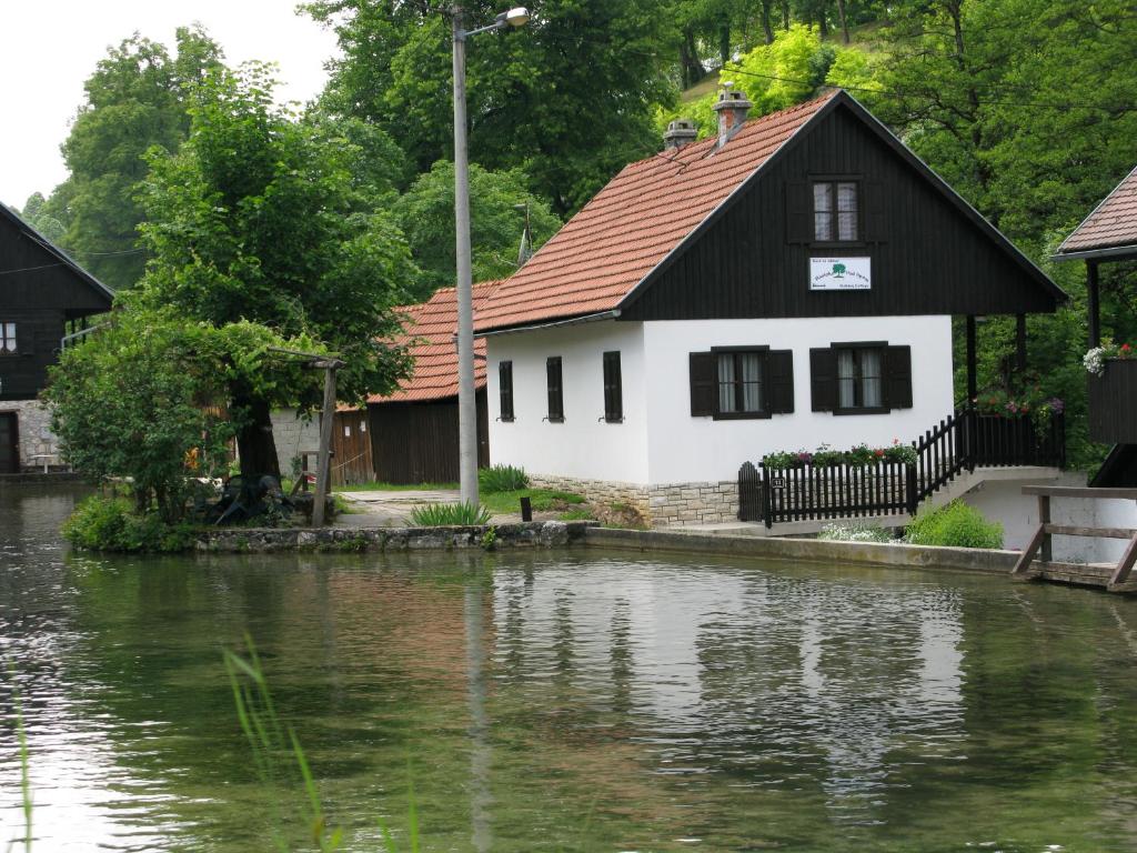 a white house with a red roof next to a river at Holiday House Rastoke Pod Lipom in Slunj