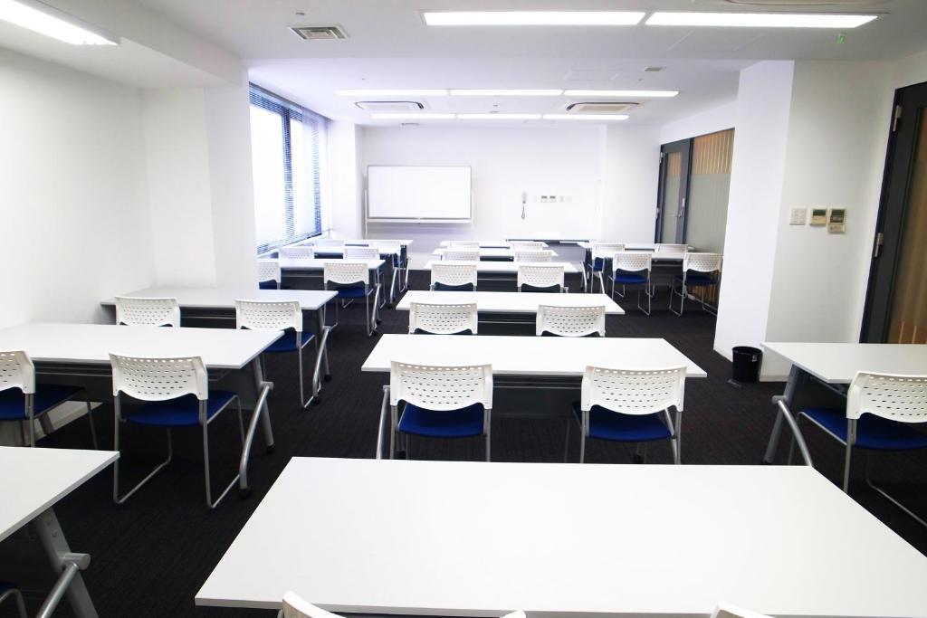 an empty classroom with white tables and chairs at HOTEL MYSTAYS Ochanomizu Conference Center in Tokyo
