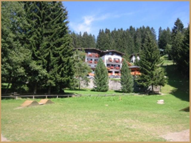 a building in the middle of a field with trees at Hotel Touring in Madonna di Campiglio