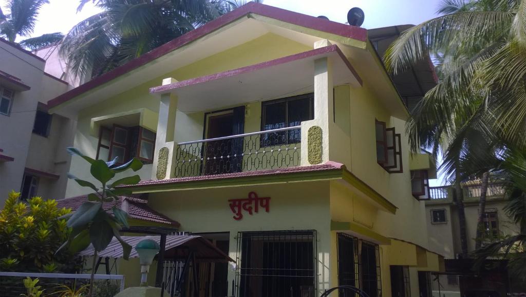 a yellow house with a balcony and palm trees at Sudeep Bungalow in Alibaug