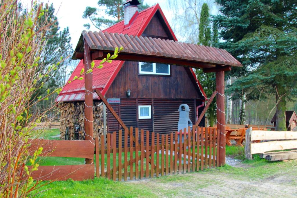 a small wooden house with a red roof behind a fence at Domek Zalesie in Barczewo