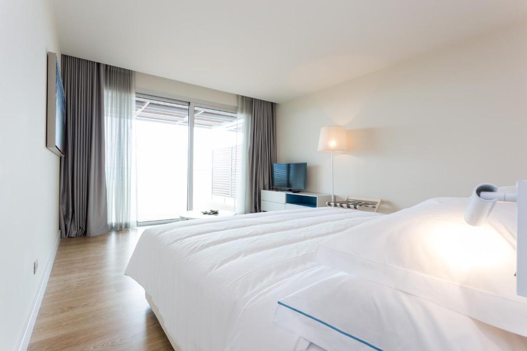 a white bedroom with a large white bed and a window at Palmares Beach House Hotel - Adults Only in Lagos