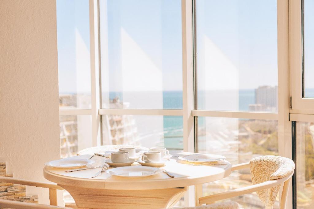 a table with cups and saucers in front of a window at Arcadia Apartment Gagarin plaza in Odesa