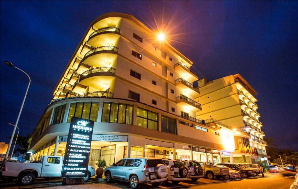 un grand bâtiment avec des voitures garées devant lui dans l'établissement Mikhael's Hotel, à Brazzaville
