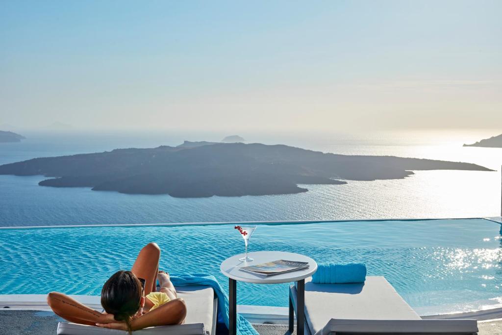 een vrouw op een stoel naast een zwembad bij Cosmopolitan Suites - Small Luxury Hotels of the World in Fira