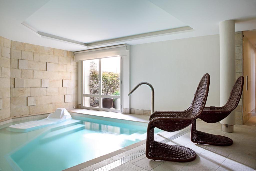 a swimming pool with two chairs in a room at Artesa Suites & Spa in Santo Tomé del Puerto