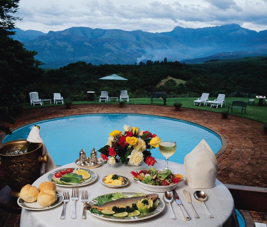a table with plates of food next to a swimming pool at Coach House Hotel & SPA Tzaneen in Tzaneen