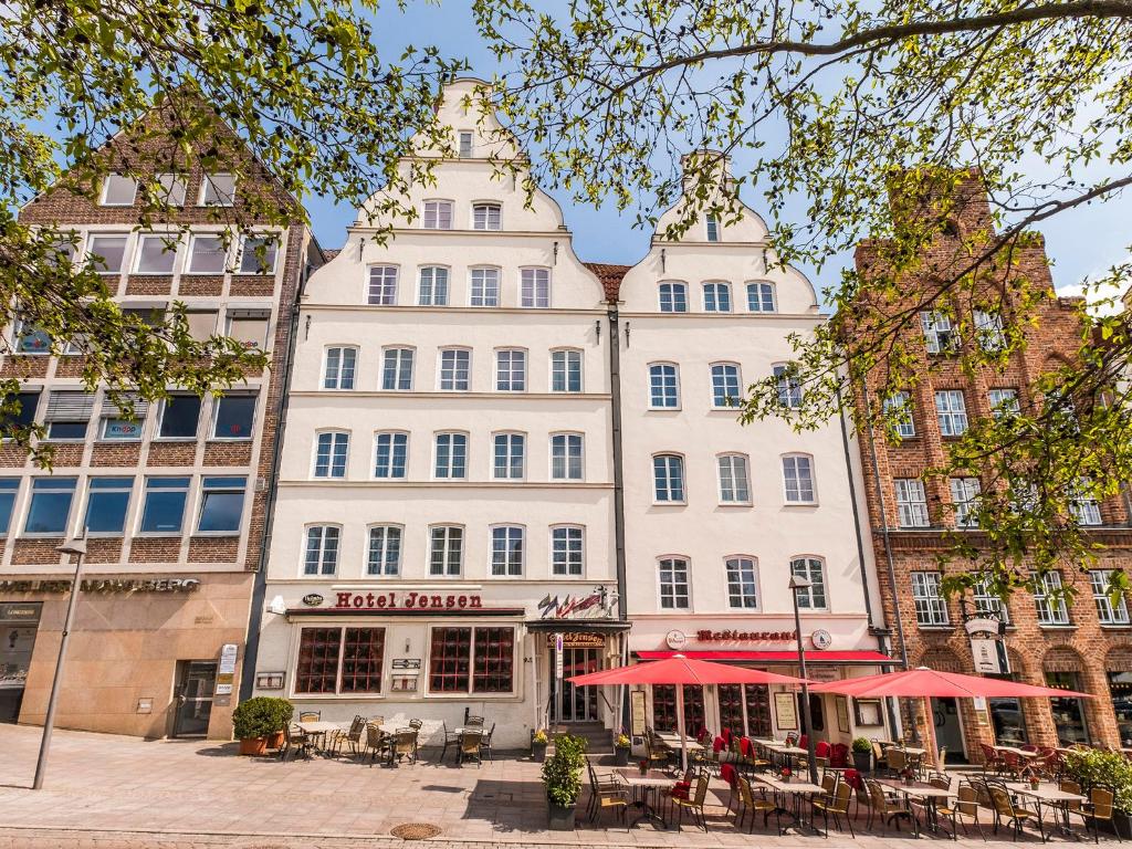 ein großes weißes Gebäude mit Tischen und roten Sonnenschirmen in der Unterkunft Ringhotel Jensen in Lübeck