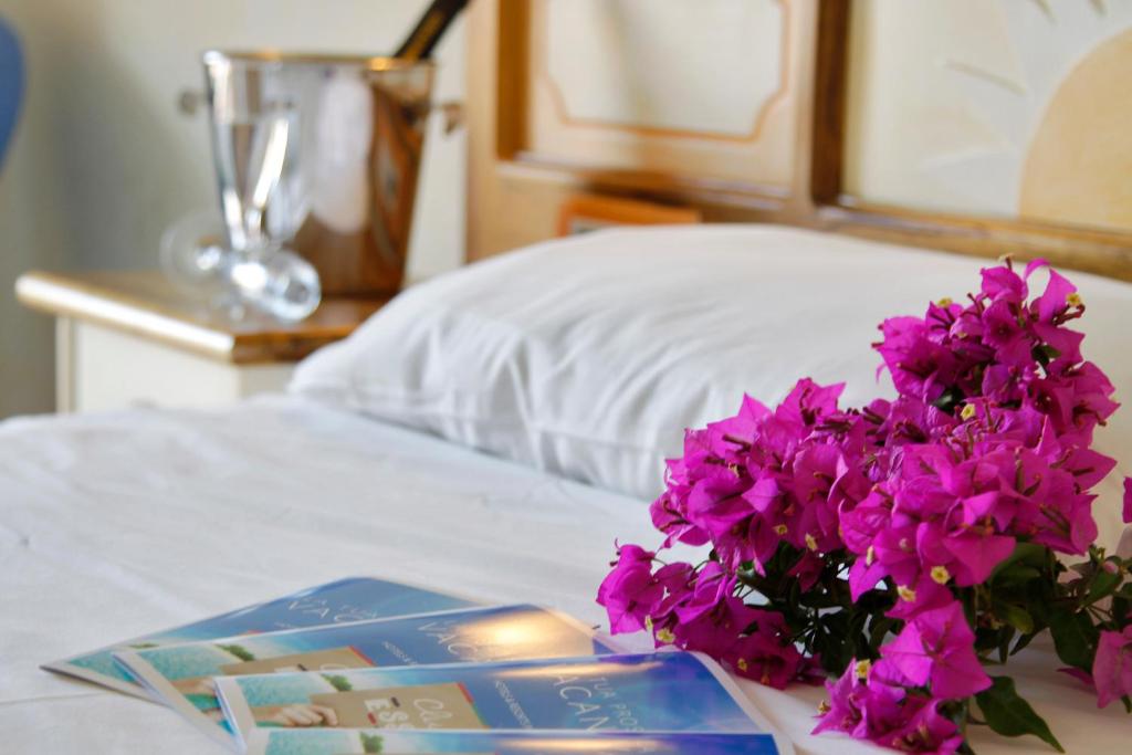 uma cama com um livro e flores roxas em Club Esse Posada em Palau