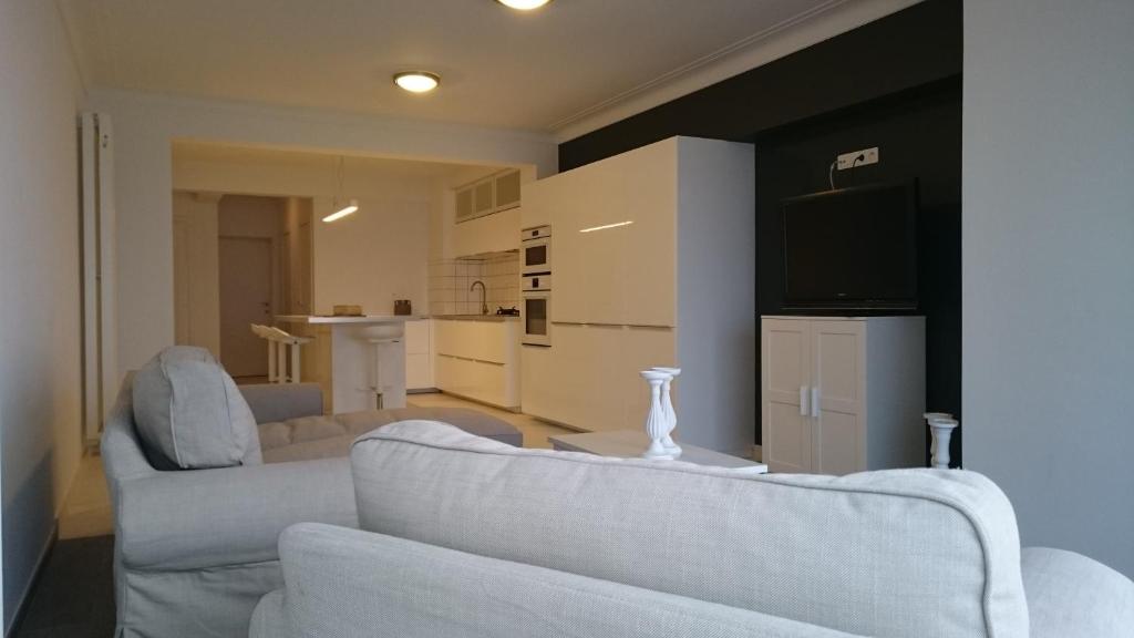 a living room with two white couches and a kitchen at lounge appartement zeedijk Oostende in Ostend