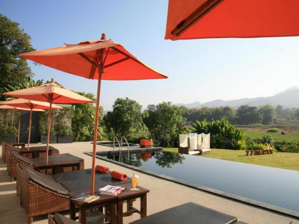 a patio with tables and umbrellas next to a pool at Yoma Hotel, Pai in Pai