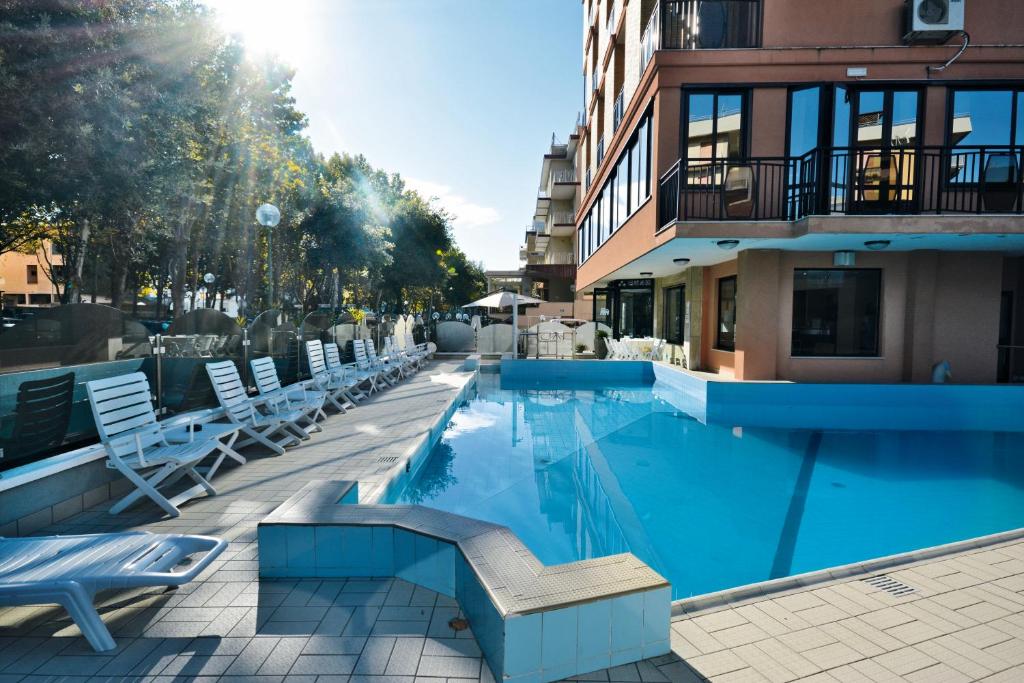 a swimming pool with lounge chairs and a building at Hotel Apollo in Cesenatico