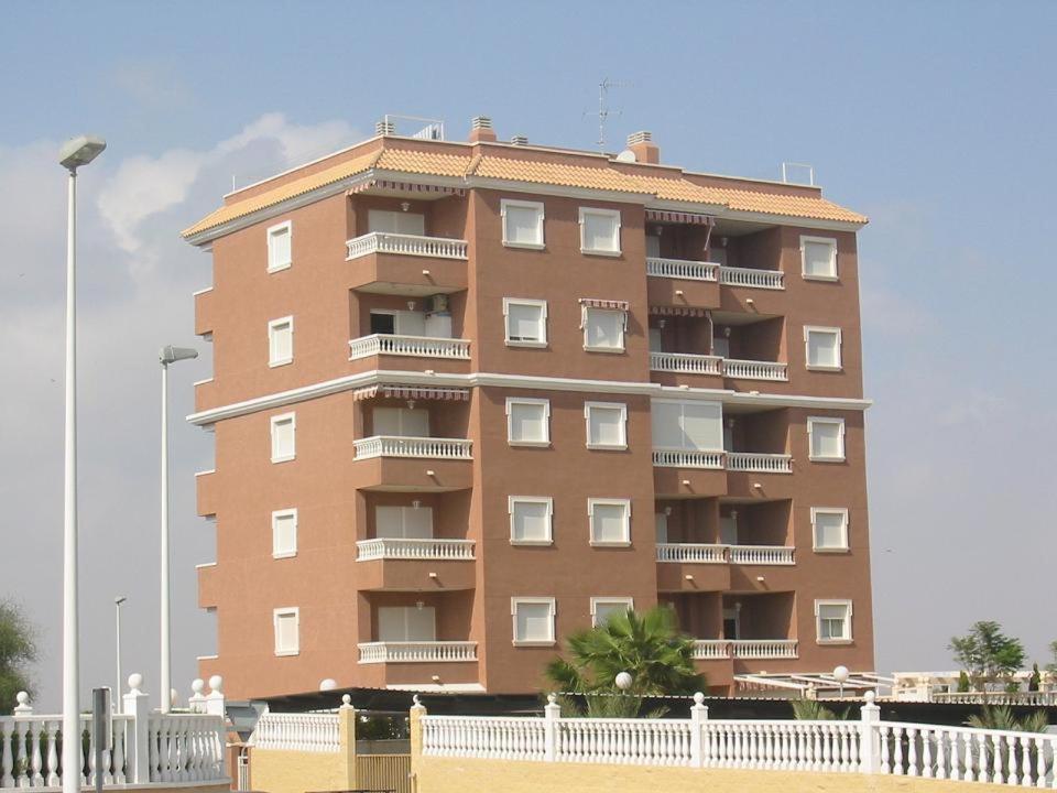 un edificio alto de color marrón con balcones y una valla blanca en Apartamentos Arenales Del Sol III, en Arenales del Sol