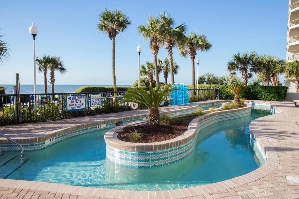 a swimming pool with palm trees and the ocean at Grande Shores in Myrtle Beach