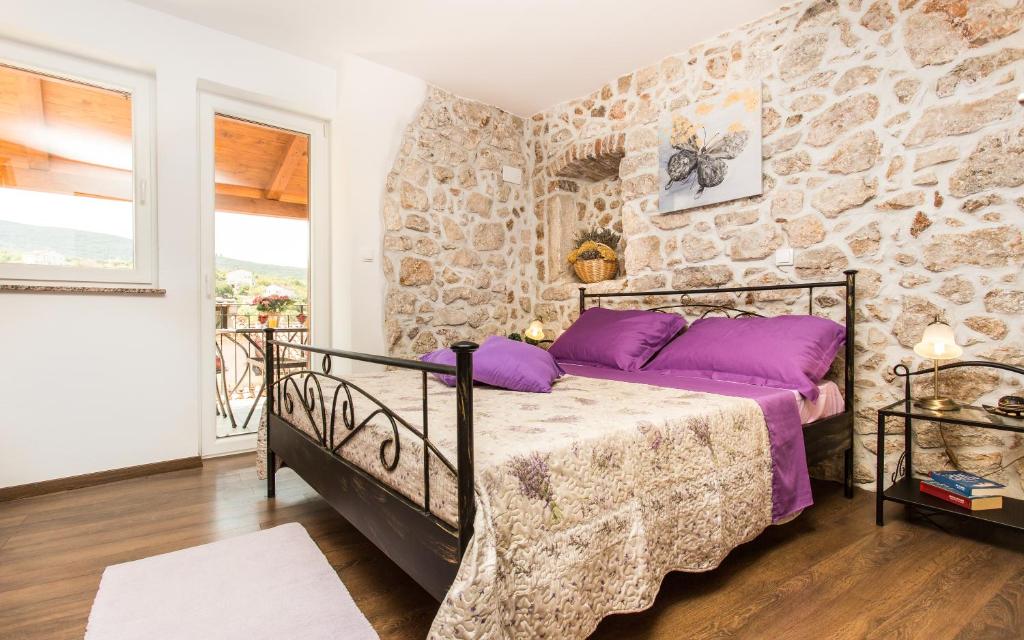 a bedroom with a stone wall and a bed with purple pillows at Apartment & Room Antonio in Vrbnik