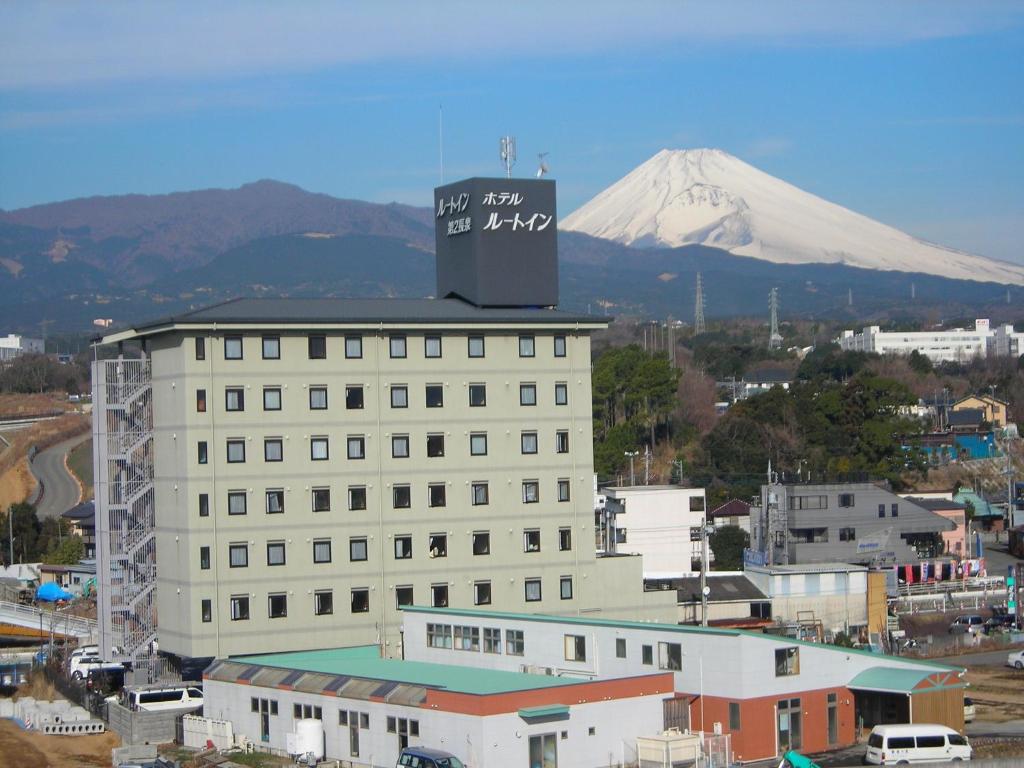 a large white building with a mountain in the background at Hotel Route-Inn Nagaizumi Numazu Inter 2 in Nagaizumi